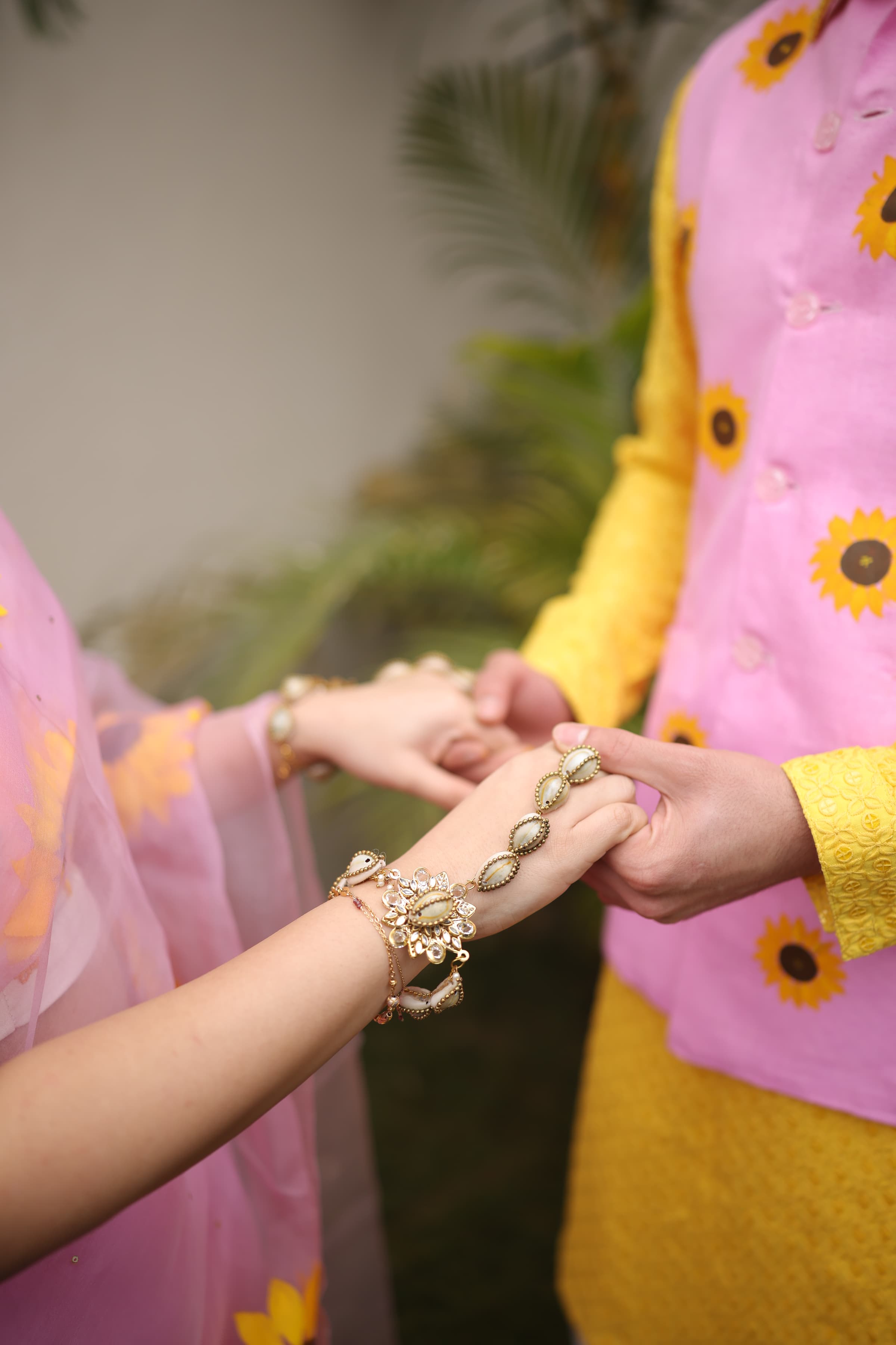 A close-up of shell-shaped haldi jewelry on the bride's wrist, hands clasped in yellow and pink
