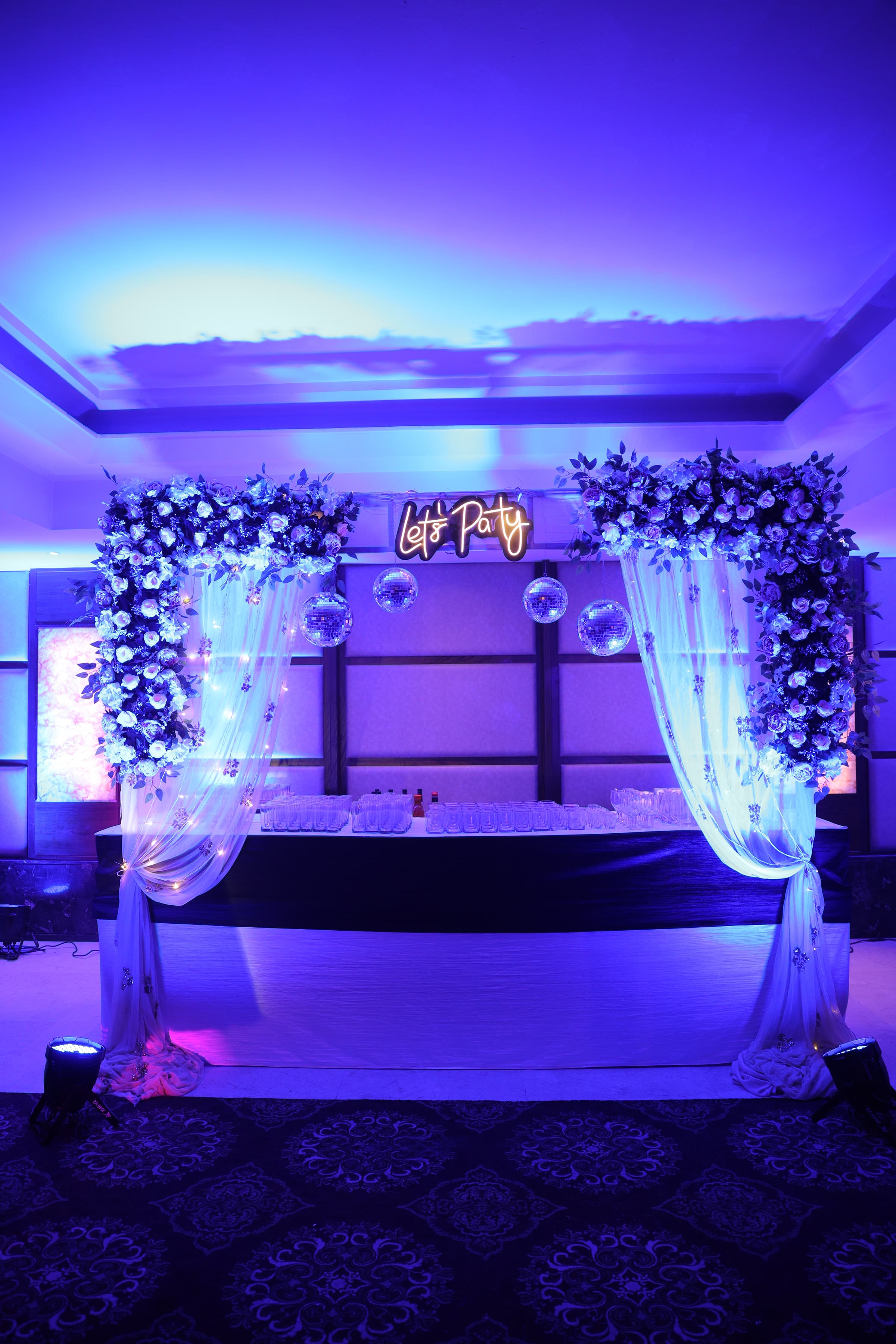 A blue floral archway with disco balls and a glowing 'Let's Party' neon sign