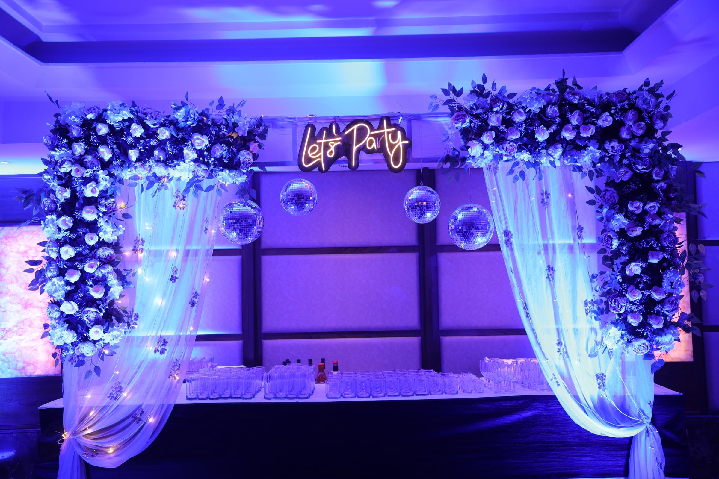 A Let's Party neon sign above hanging disco balls