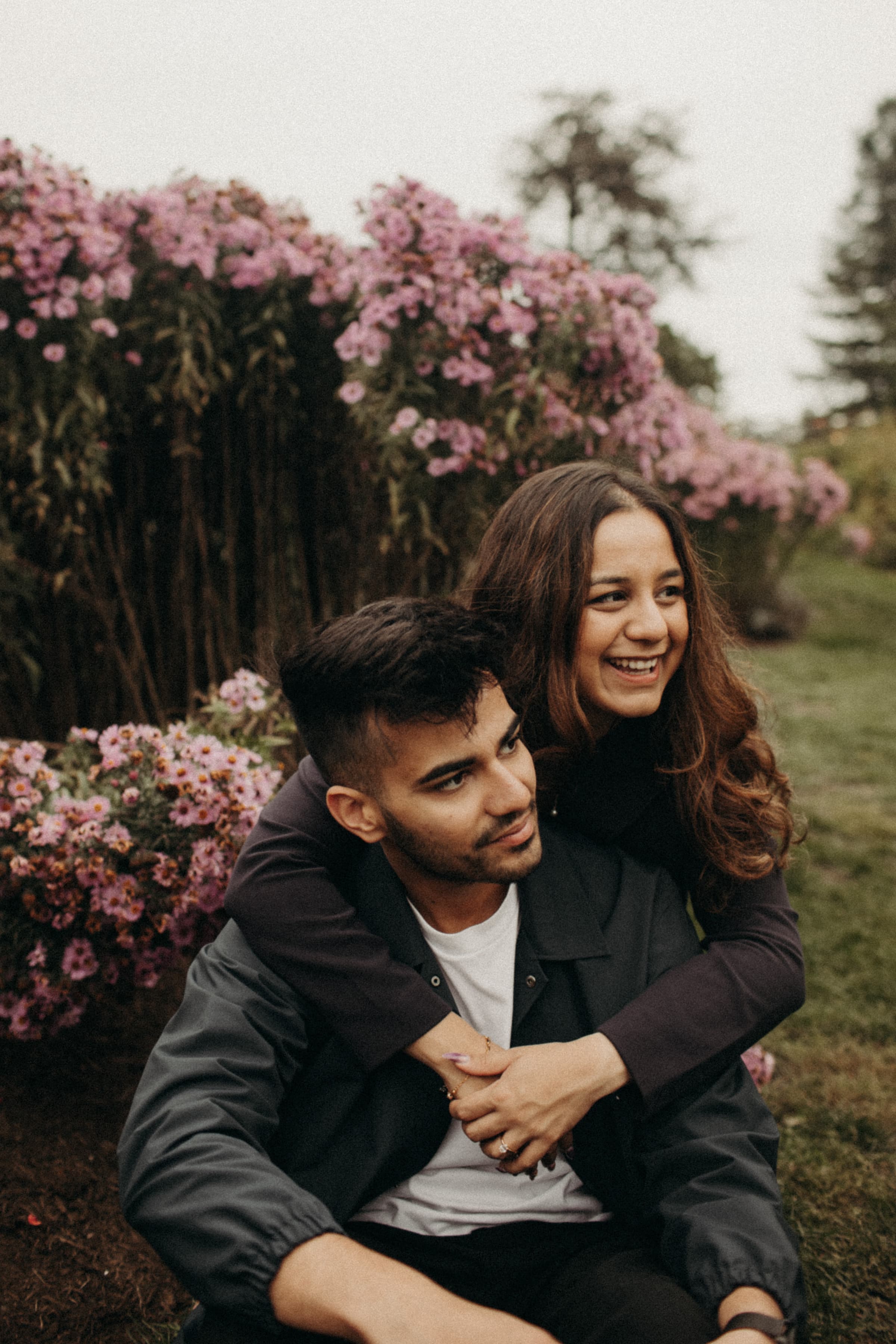 Sakina embracing Aayush from behind in a garden of pink flowers, both laughing