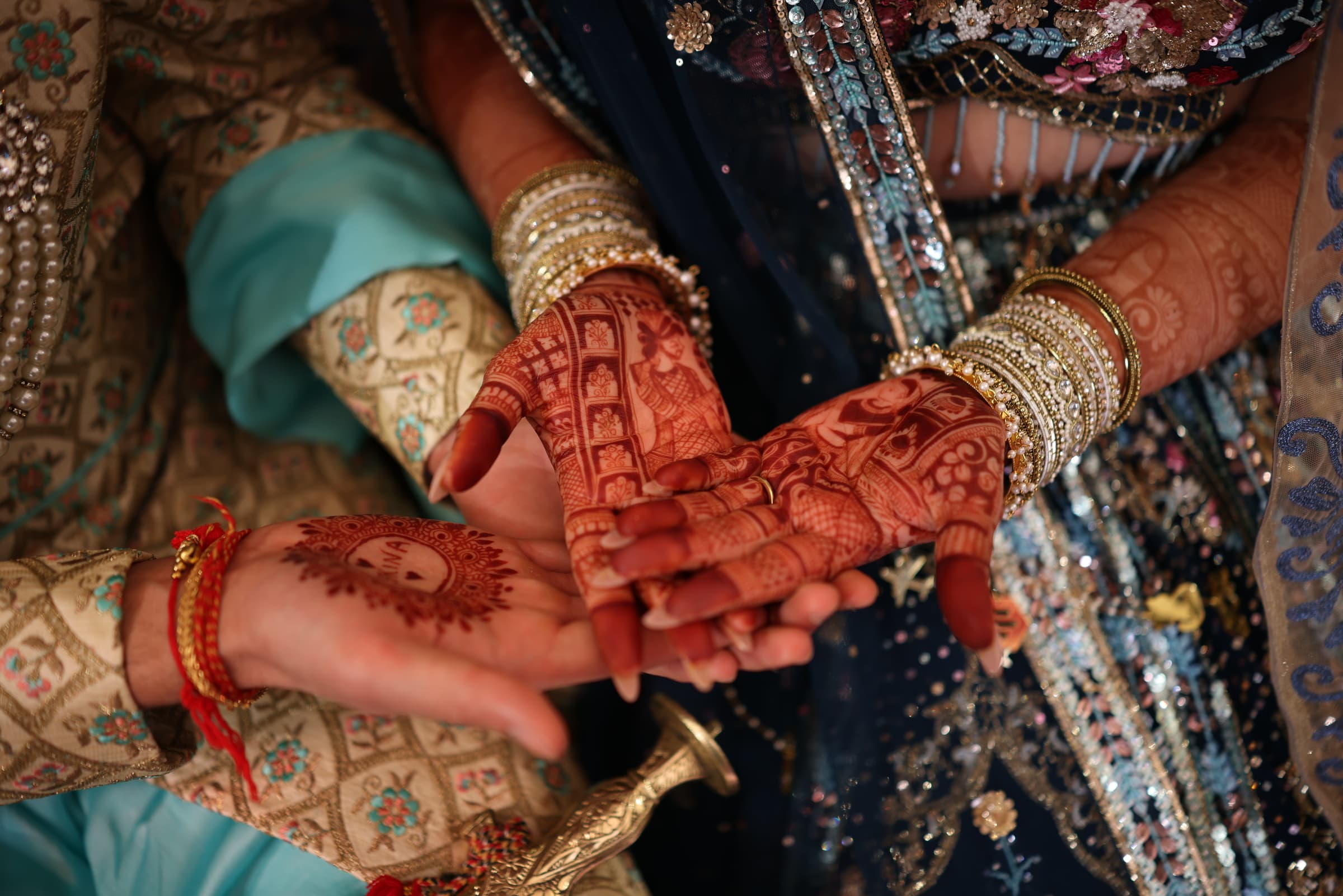 The couple's henna-painted hands clasped together, bangles and bridal embroidery in close-up