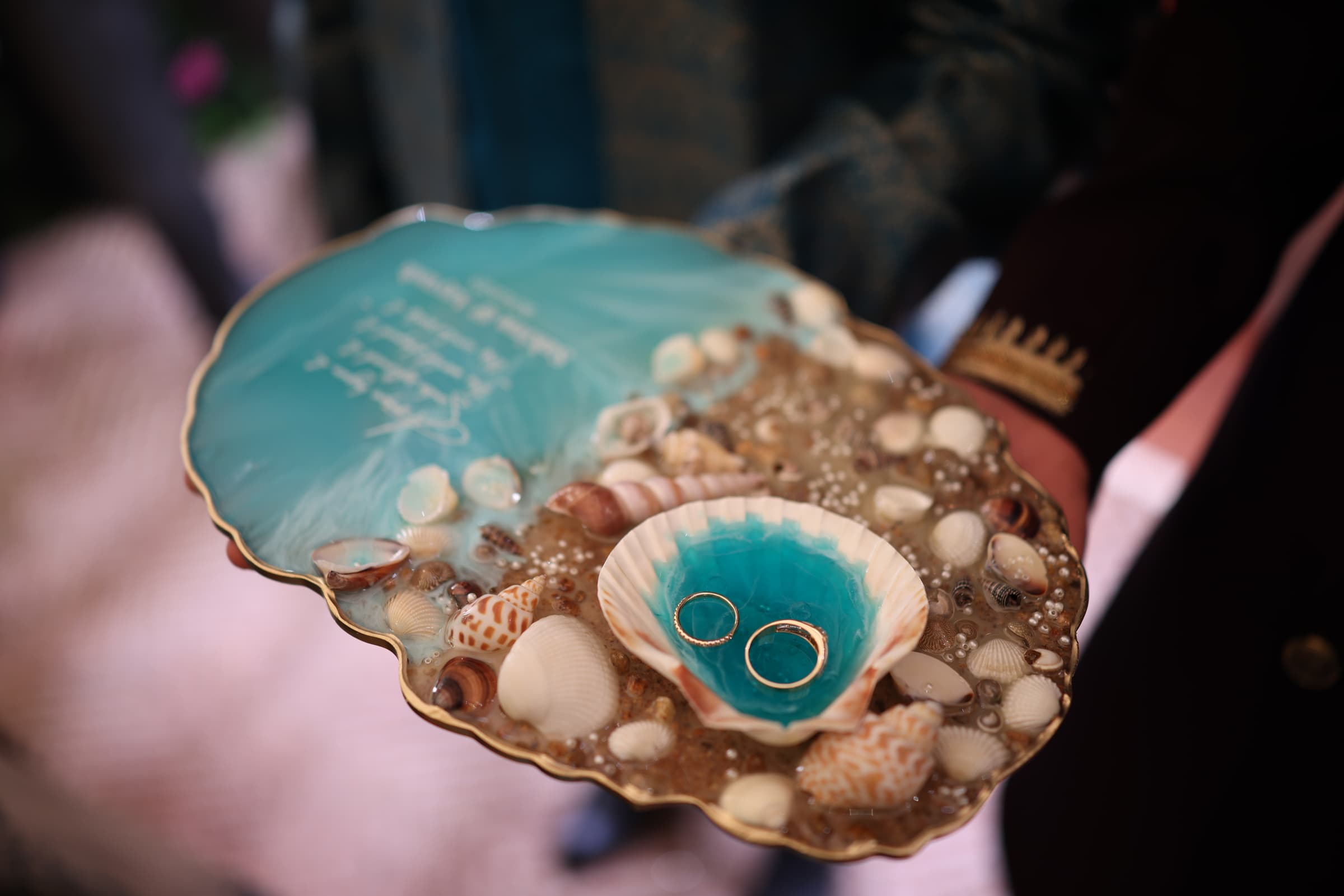 The ocean-themed ring platter, rings nestled in a shell on turquoise resin surrounded by seashells