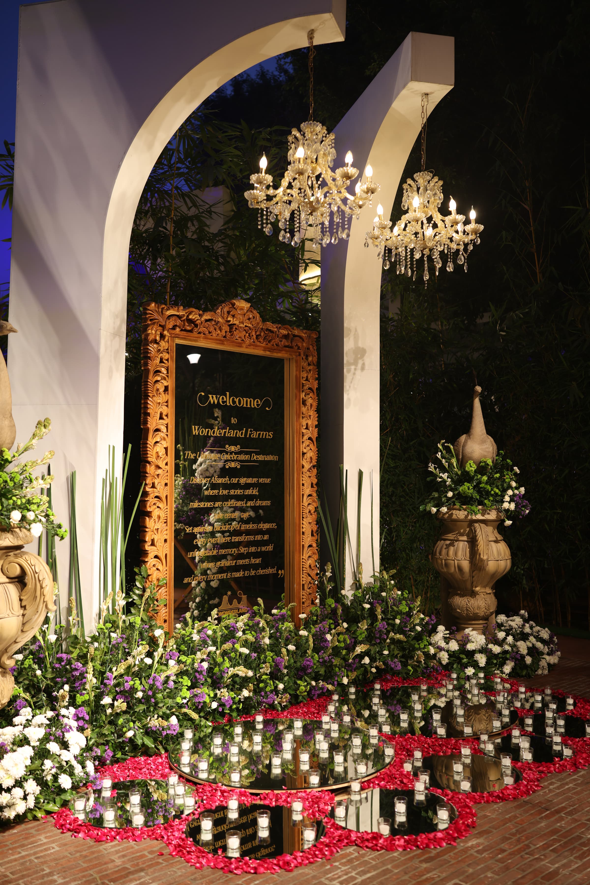 The Welcome to Wonderland Farms sign in a carved wooden frame, flanked by florals and crystal chandeliers